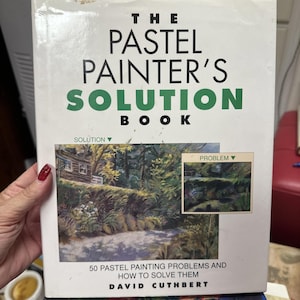 Puede incluir: Un libro titulado "The Pastel Painter's Solution Book" con texto verde y negro. La portada presenta una pintura de paisaje con una pequeña imagen insertada. El subtítulo del libro dice "50 Pastel Painting Problems and How to Solve Them."