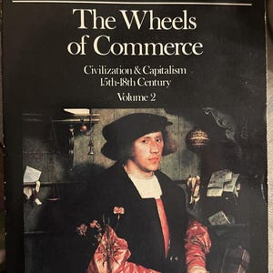 May include: Book cover for "The Wheels of Commerce" by Fernand Braudel. The cover features a portrait of a man in a black coat and hat, with text in red and white. The book is Volume 2 of Civilization & Capitalism.