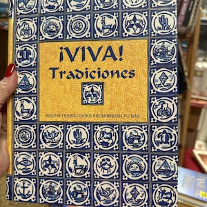 May include: A yellow and blue cookbook titled "¡VIVA! Tradiciones" with the subtitle "South Texas Cooks from Brush to Bay". The cover features a repeating pattern of blue and white tiles with various images.