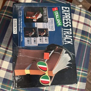 May include: A vintage language learning kit titled "Express Track to Italian." The box features a book illustration, cassette tapes, and the text "A Teach-Yourself Program." The cover includes the Barron's logo and the price.