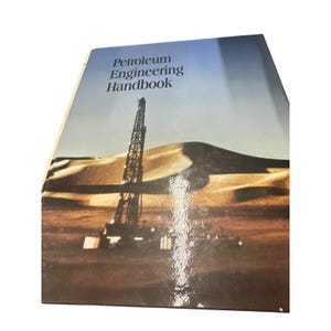 Puede incluir: Un libro de tapa dura titulado "Petroleum Engineering Handbook". La portada presenta un paisaje desértico con una plataforma de perforación y una duna de arena. El cielo transita del azul al marrón claro.