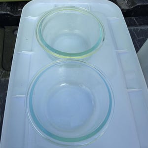 Puede incluir: Dos cuencos de vidrio transparente con un tinte azul claro, colocados sobre una bandeja de plástico blanco. Los cuencos son redondos con un borde ligeramente ensanchado. La bandeja tiene una superficie texturizada y bordes elevados.