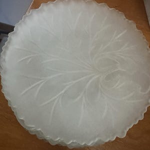 May include: A stack of frosted glass plates with a scalloped edge. Each plate features a delicate, etched leaf design radiating from the center. The plates are a soft white color, and appear to be vintage or antique.
