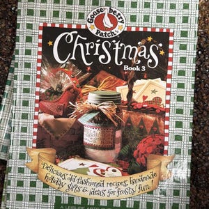 Könnte beinhalten: Weihnachtsbuch 3 von Gooseberry Patch. Das Cover zeigt ein festliches Design mit einem Glas Schokoladen-Keksmischung, einem rot-grünen Karomuster und dem Text "Delicious old-fashioned recipes, handmade holiday gifts & ideas for frosty fun!"