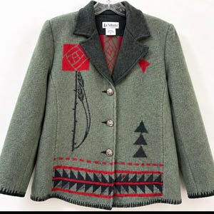 May include: A sage green jacket with a dark gray collar and three silver-toned buttons. The front features a red square, a black feather-like design, three black triangles, and a bottom border of black and red geometric patterns.