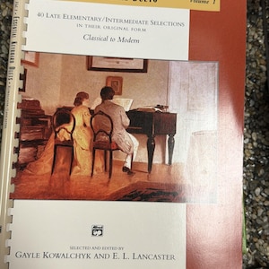 May include: A book titled "Essential Keyboard Duets, Volume 1" with a cover illustration of two people playing a piano. The book is edited by Gayle Kowalchyk and E. L. Lancaster. The cover has a red and white colour scheme.