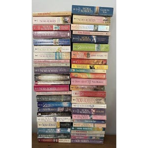 May include: A stack of paperback books by Nora Roberts. The books have colorful covers with titles like "Close to You," "River's End," and "Summer Pleasures." The spines display the author's name and book titles.