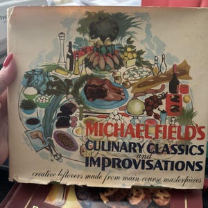 Puede incluir: Una portada de libro de cocina vintage con una ilustración colorida de una mesa puesta con comida, vino y otros artículos. El título del libro es "MICHAEL FIELD'S CULINARY CLASSICS and IMPROVISATIONS creative leftovers made from main-course masterpieces".