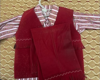Op de afbeelding: Een rode suède vest- en broekenset met franjedetails. Het vest heeft een decoratief patroon op de kraag en de mouwen zijn voorzien van rode, witte en gouden strepen. De broek is effen rood van kleur.
