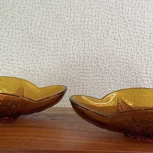Pode incluir: Duas tigelas de vidro âmbar com borda festonada e design texturizado. As tigelas estão sobre uma superfície de madeira.