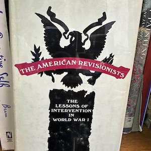 May include: A book titled "The American Revisionists" with a black eagle graphic and red banner. The book cover also includes the text "The Lessons of Intervention in World War I" and the author's name, Warren I. Cohen.