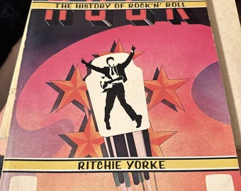 Könnte beinhalten: Ein Vintage-Buch mit dem Titel "The History of Rock'n'Roll" von Ritchie Yorke. Das Cover zeigt eine Silhouette eines Musikers mit Gitarre vor einem rosa-orangenen Hintergrund mit Sternen. Das Wort "ROCK" ist in fetten roten Buchstaben geschrieben.