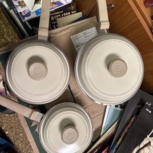 Puede incluir: Tres ollas de cocina de cerámica blanca con asas negras. Las ollas tienen un borde negro y el texto "CLUB SUPRA" impreso en la parte inferior.