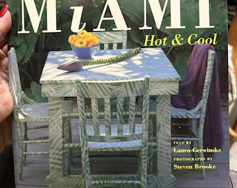 May include: A book cover with the title "Miami Hot & Cool" featuring a table and chairs painted with a green and white leaf pattern. The text "Text by Laura Cerwinske" and "Photographs by Steven Brooke" is printed on the cover.