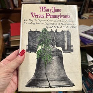 Può includere: Un libro intitolato "Mary Jane Versus Pennsylvania: The Day the Supreme Court Heard the Arguments for and against the Legalization of Marijuana." di Ralph Adam Fine. La copertina presenta una pianta di marijuana verde che cresce dalla Liberty Bell.