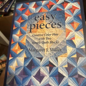 May include: A book titled "easy pieces" with a geometric quilt pattern design in shades of blue, orange, and purple. The cover text reads "Creative Color Play with Two Simple Quilt Blocks" by Margaret J. Miller.