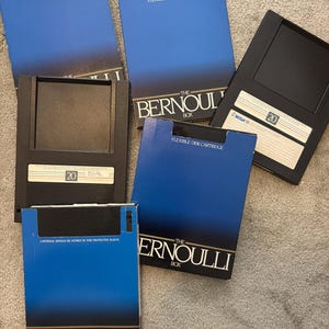 May include: A collection of vintage Iomega Bernoulli Box flexible disk cartridges. The boxes are blue and black, with white text that reads "FLEXIBLE DISK CARTRIDGE" and "THE BERNOULLI BOX". Some cartridges have the number "20" on them.