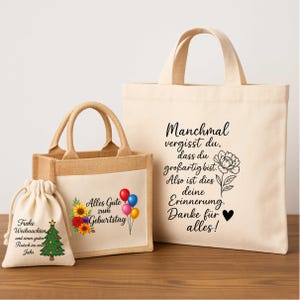 May include: A set of three beige tote bags with various printed designs. One bag has text and a floral design, another says "Alles Gute zum Geburtstag" with balloons and flowers, and the last has a Christmas tree.