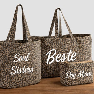 Könnte beinhalten: Drei Tragetaschen und eine kleine Tasche mit Leopardenmuster. Die größte Tragetasche trägt den weißen Schriftzug "Beste". Die andere Tragetasche trägt den Schriftzug "Soul Sisters". Die Tasche trägt den Schriftzug "Dog Mom".