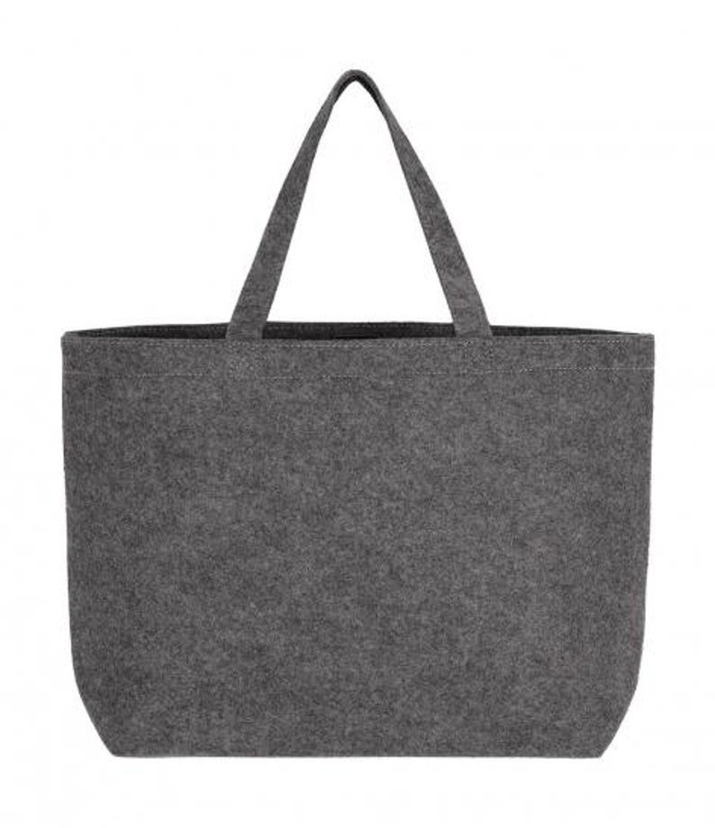 May include: A gray tote bag with two handles. The bag is made of a felt-like material and has a rectangular shape with rounded corners. The handles are attached to the top of the bag and are the same color as the bag.