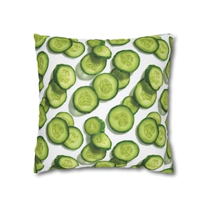 May include: Square cushion featuring a repeating pattern of green cucumber slices against a white backdrop. The cushion has a soft appearance, ideal for adding a fresh touch to any room. The design is simple and modern, suitable for any decor.