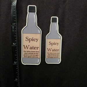May include: Two stickers shaped like bottles, one large and one small, with a gray body and black cap. The label reads "Spicy Water" with additional text below. The larger sticker is approximately 3 inches tall.
