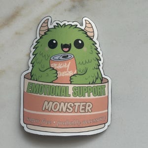 Może przedstawiać: Naklejka przedstawiająca zielonego potwora z rogami trzymającego puszkę napoju "Peachy Energy". Naklejka głosi "EMOTIONAL SUPPORT MONSTER" i "bez cukru &bull; prawdopodobnie konieczne" w stylu kresk&oacute;wkowym.