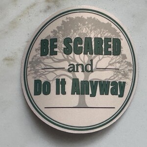 Może przedstawiać: Okrągła naklejka z jasnobeżowym tłem i zieloną obw&oacute;dką. Naklejka zawiera grafikę drzewa i tekst "BE SCARED and Do It Anyway" w zielonych literach.