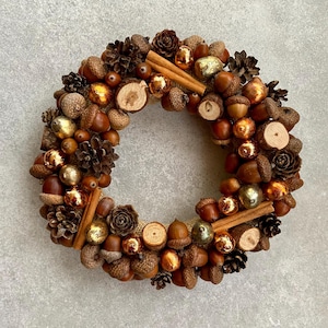 May include: A brown and gold autumnal wreath decorated with acorns, pinecones, cinnamon sticks, and gold ornaments.