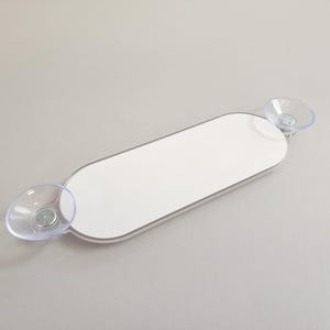 May include: White oval-shaped bathroom shelf with two suction cups on either end. The shelf is designed to be mounted on a smooth surface.