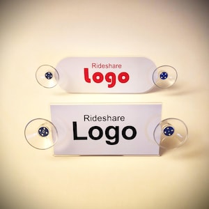 May include: Two white rectangular signs with the words "Rideshare Logo" printed on them. The top sign has the word "Logo" in red. Each sign has two clear suction cups attached.