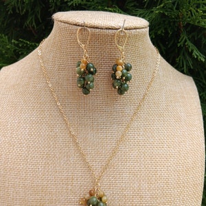 May include: A gold chain necklace and matching earrings with a cluster of green and gold beads. The beads are arranged in a grape-like shape.