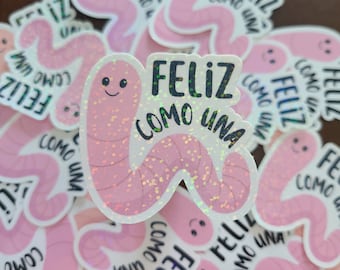 May include: A pink glitter sticker with a worm design and the text "Feliz como una" in black. The sticker is surrounded by other stickers with similar designs.