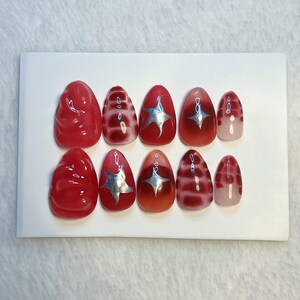 May include: Set of ten red and silver press-on nails with different designs. Some nails have a swirl design, some have a star design, and some have a striped design.