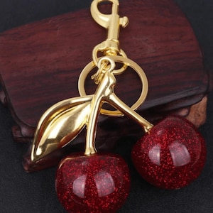 May include: Gold cherry keychain with red glitter cherries and a gold chain and clasp.