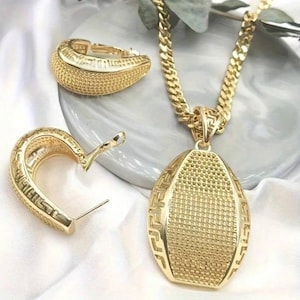 Op de afbeelding: Een goudkleurige sieradenset met een ketting met een grote hanger, een paar oorringen en een bijpassende armband. De set heeft een getextureerd oppervlak en een geometrisch ontwerp. De ketting heeft een dikke ketting en de hanger is ovaal.