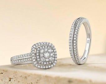May include: Two silver rings with sparkling clear stones. One ring features a square halo design with a central cluster of stones, while the other is a band with stones set around the entire circumference. The rings are displayed on a neutral surface.