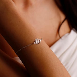 May include: A delicate silver bracelet featuring a small, stylized planet charm. The bracelet is worn on an arm, with the charm positioned near the wrist. The design is minimalist and elegant, suitable for everyday wear. The bracelet's chain is fine and subtle.
