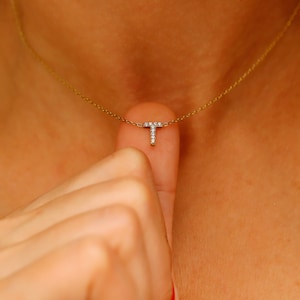 May include: A gold chain necklace with a small diamond letter T pendant.