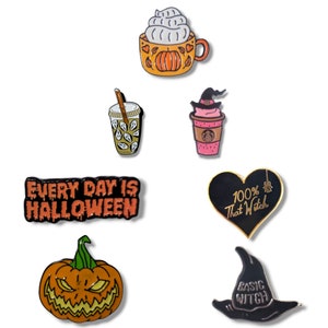 Könnte beinhalten: Eine Sammlung von Halloween-Emaille-Anstecknadeln. Designs umfassen einen Pumpkin Spice Latte, einen Hexenhut, einen Kürbis und den Satz "Every Day Is Halloween". Die Anstecknadeln weisen leuchtende Farben und komplizierte Details auf.