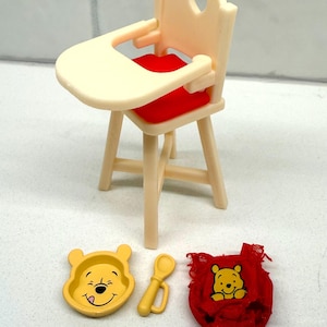 May include: A miniature Winnie the Pooh themed high chair set. The set includes a cream-colored high chair with a red seat, a yellow bowl, a yellow spoon, and a red bib. The bowl and bib feature Winnie the Pooh's face.