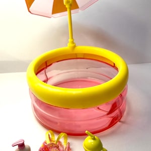 May include: A miniature playset featuring a pink and yellow swimming pool with a yellow parasol. Accessories include a swimsuit, sunscreen, and a yellow drink cup. The set is designed for imaginative play.