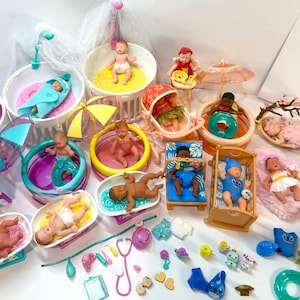 May include: A collection of miniature baby dolls in various settings, including bathtubs, beds, and pools. The dolls are in different poses and outfits, with accessories like umbrellas and toys. The color palette includes pink, blue, yellow, and white.