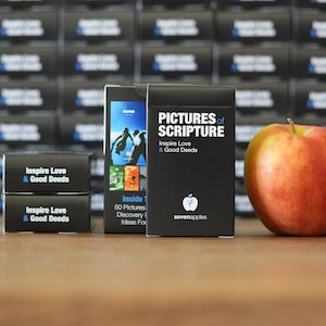 May include: A set of black and white playing cards with the text "Pictures of Scripture" and "Inspire Love & Good Deeds" on the front. The cards are stacked on a wooden table next to a red apple.