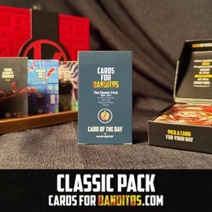 May include: A dark blue box of "Cards for Banditos" with the text "The Classic Pack" and "Card of the Day." The box is next to an open box of cards and other card packs. The text "CLASSIC PACK CARDS FOR BANDITOS.COM" is at the bottom.