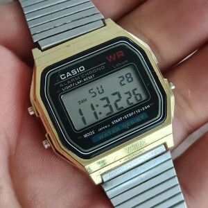 May include: A gold-toned Casio digital watch with a black face and silver band. The watch displays the time as 11:32:26 and the date as 28. The watch has the text "CASIO" and "WATER RESIST" on the face.