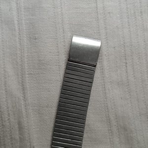 May include: A silver-toned watch band with a rectangular clasp and a flexible, expandable design. The band is composed of numerous small, rectangular metal links, creating a textured appearance. The watch band is shown against a light gray background.