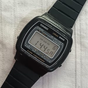 May include: A black Casio digital watch with a rectangular face. The watch displays the time 14:45 and the number 6. The watch has a black band and features the text "CASIO" and "ALARM CHRONOGRAPH".