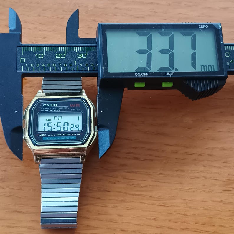May include: A gold-toned Casio digital watch with a silver band is measured with a black digital caliper. The watch face displays the time as 15:50:24. The caliper reads 33.1 mm.