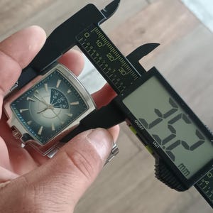May include: A silver wristwatch with a dark blue face is measured with a digital caliper. The watch face has white markers and hands. The caliper displays a measurement of 35.2 mm.
